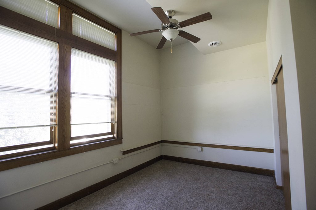 an empty room with a ceiling fan and two windows