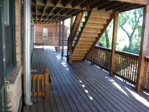 a covered deck with stairs and a brick building in the background