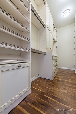 a walk in closet with white cabinets and a wood floor