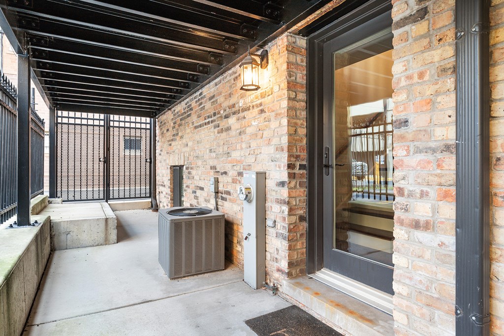 the front porch of a brick building with a trash can and a window