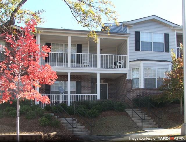 A tree with red leaves is in front of a two-story house.