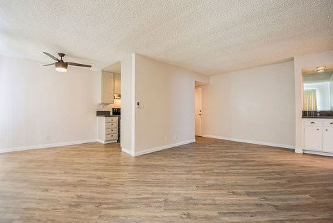 an empty living room with a ceiling fan and a kitchen