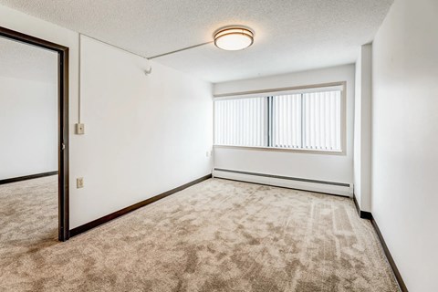 A room with a carpeted floor and a window with blinds.