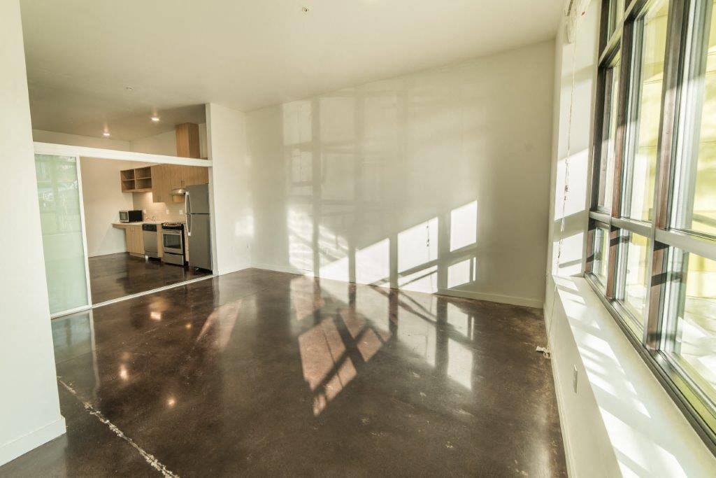 a large empty living room with windows and a concrete floor