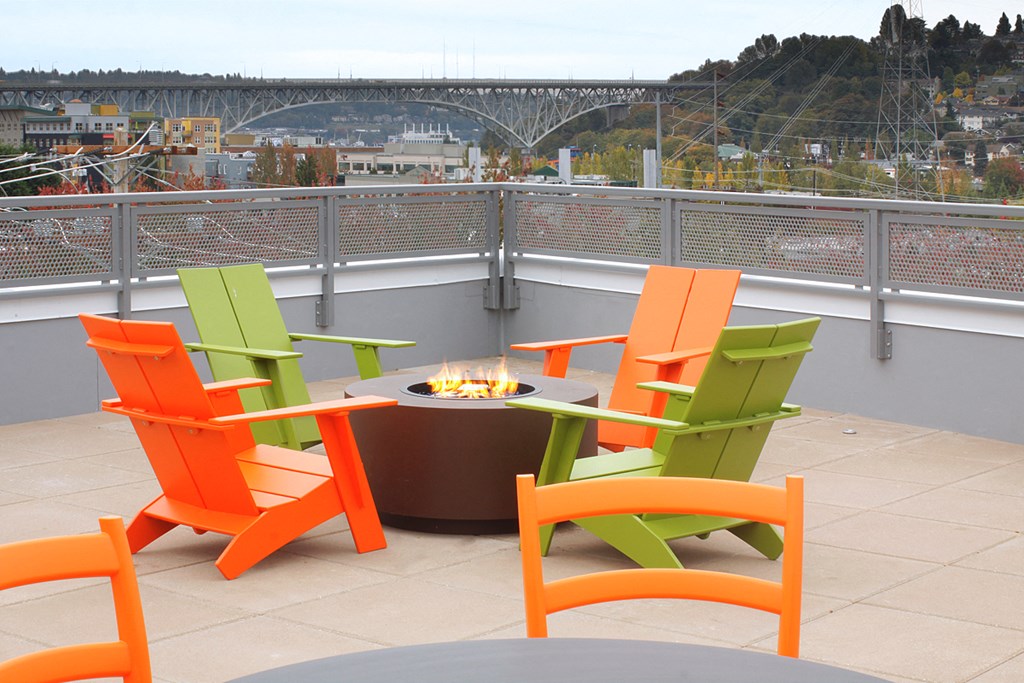 a patio with orange and green chairs and a fire pit on a roof