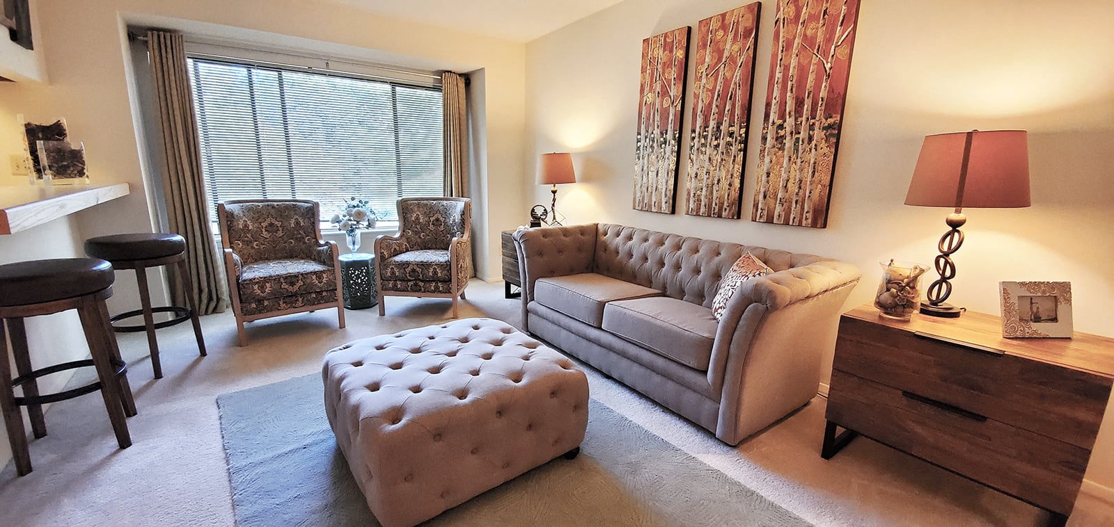 A living room with a grey couch, two chairs, a table, and a painting on the wall.