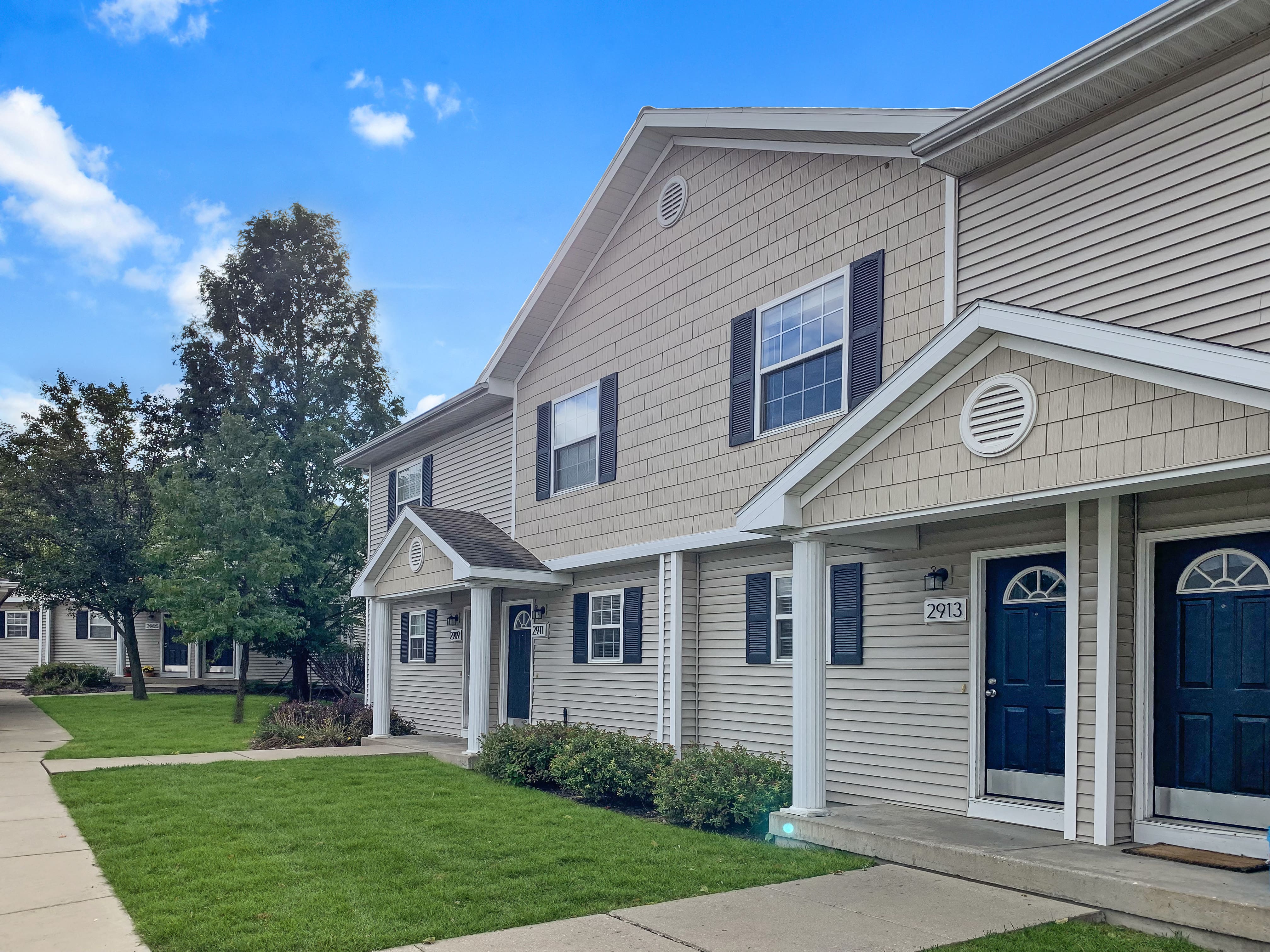 a tan house with blue doors and a green lawn