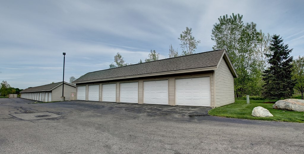 a long garage with white doors and a gravel driveway