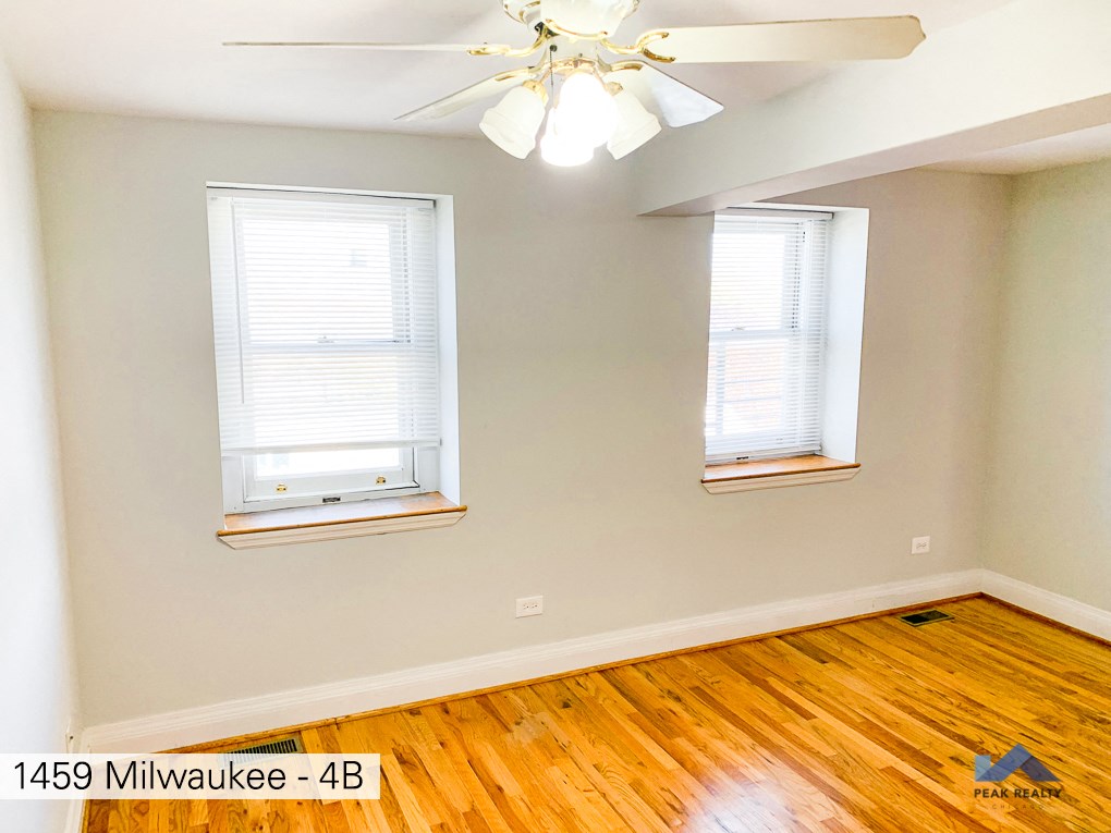 a room with a wood floor and two windows and a ceiling fan