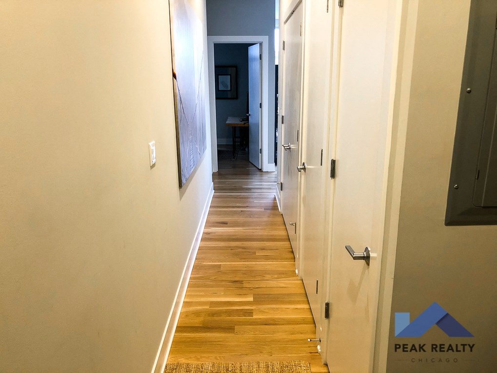 a hallway with wood flooring and white walls and a door to a bedroom