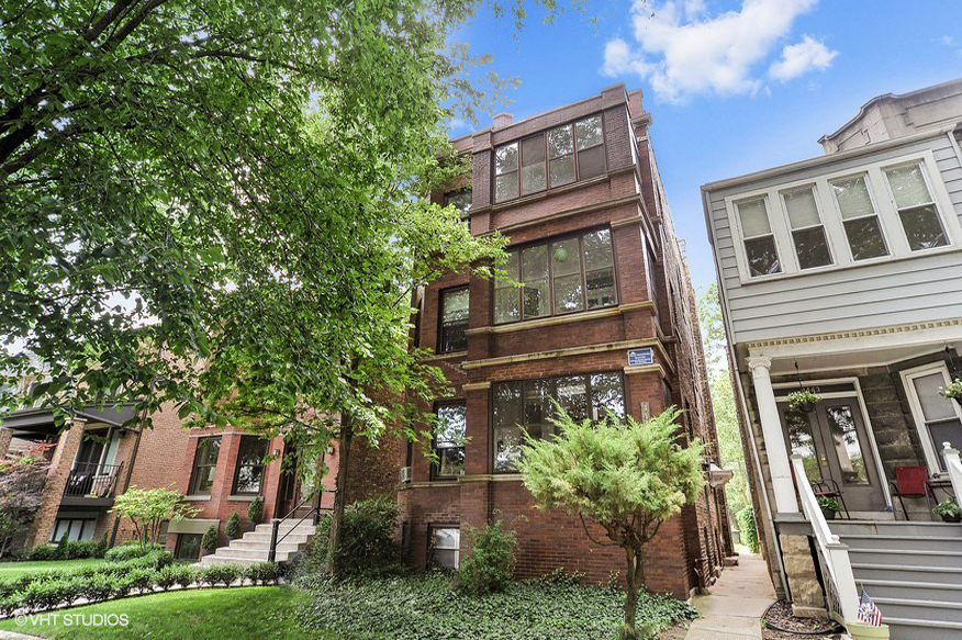 a red brick apartment building with trees and a sidewalk