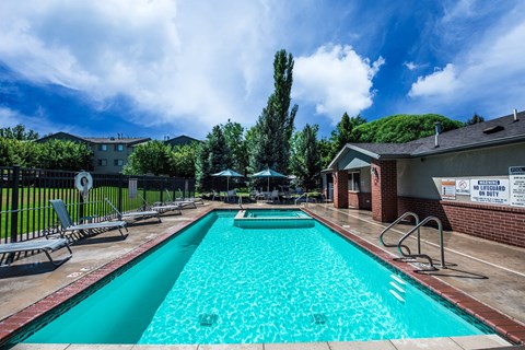 A large outdoor swimming pool with a red brick building and trees in the background.