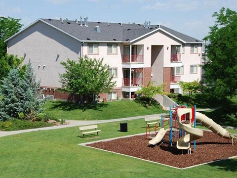 A playground with a slide and a bench in front of a building.