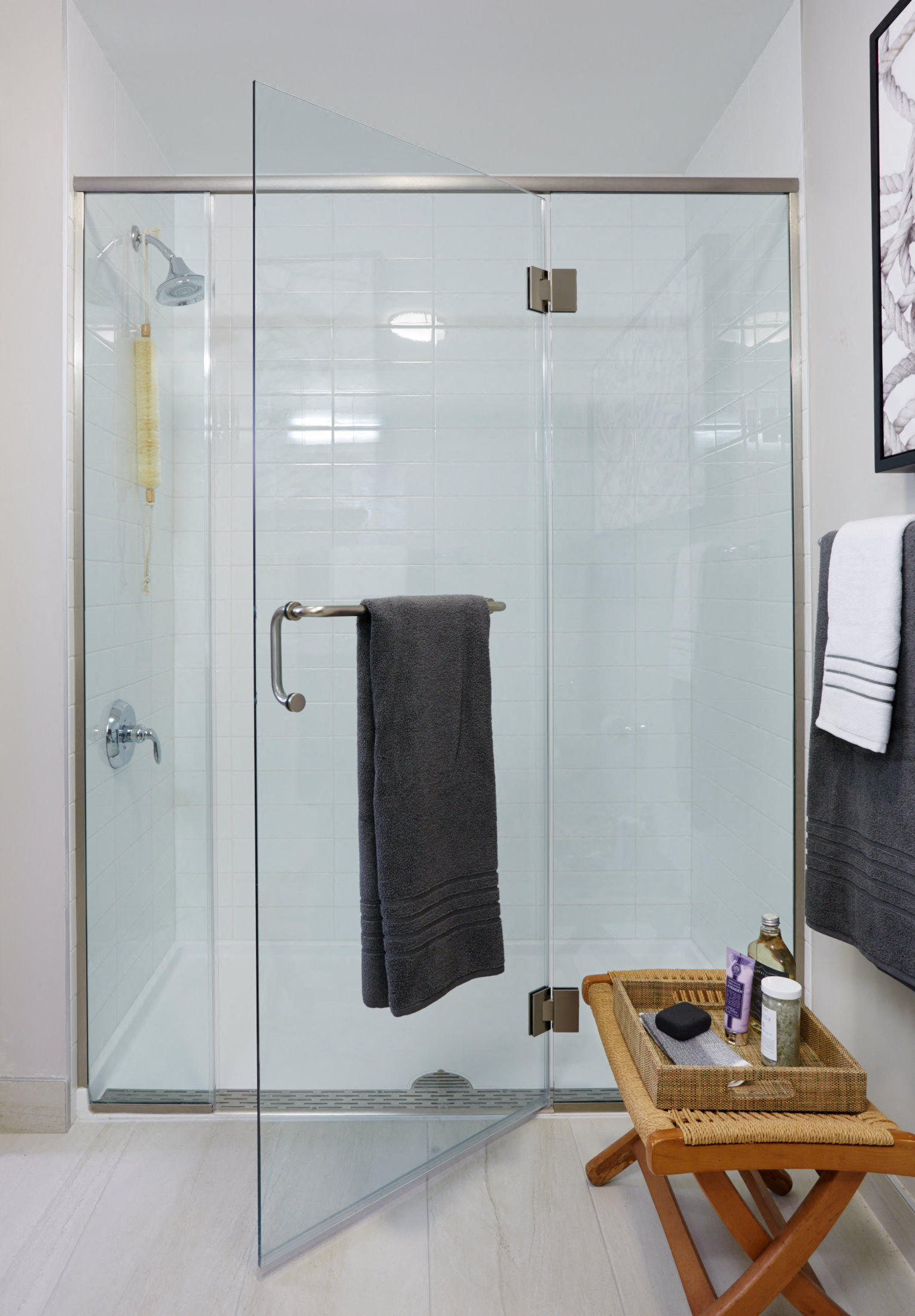 a bathroom with a shower with a glass door and a towel rack and a stool