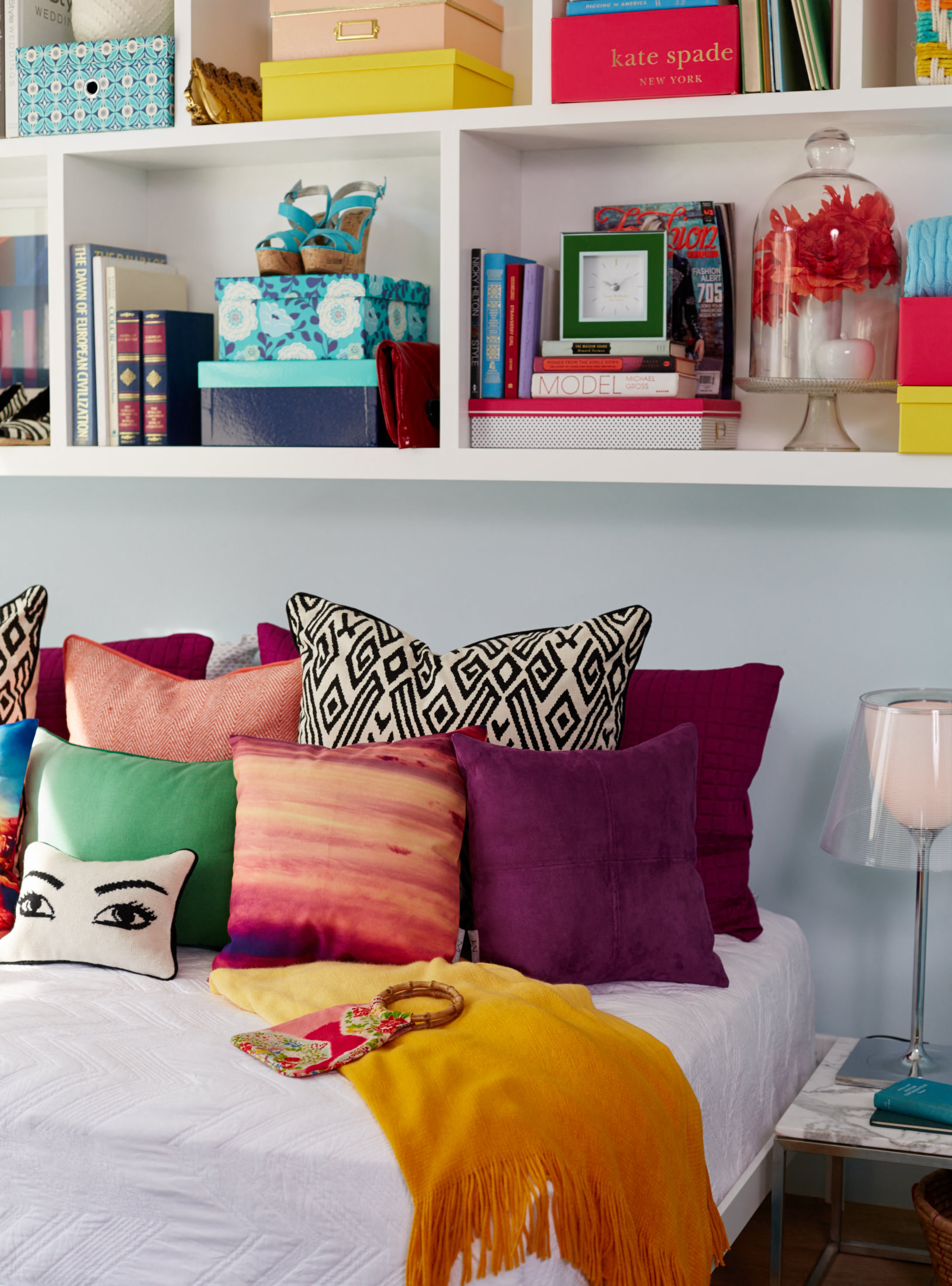 a bed with colorful pillows and a shelf with books