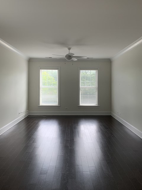an empty living room with a ceiling fan and two windows