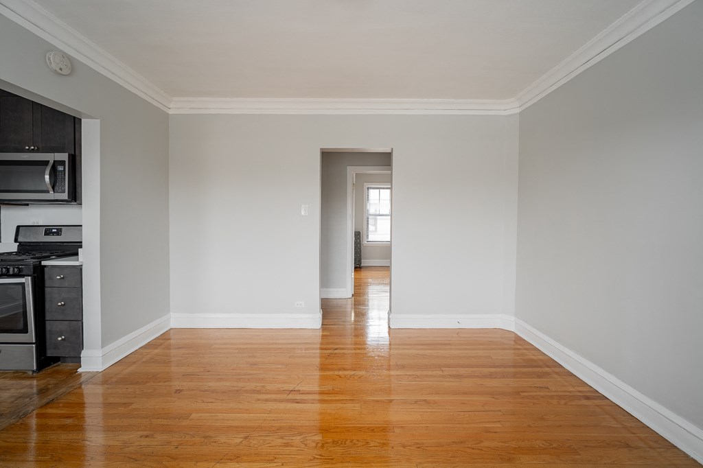 an empty living room with wooden floors and a hallway to a kitchen and a door