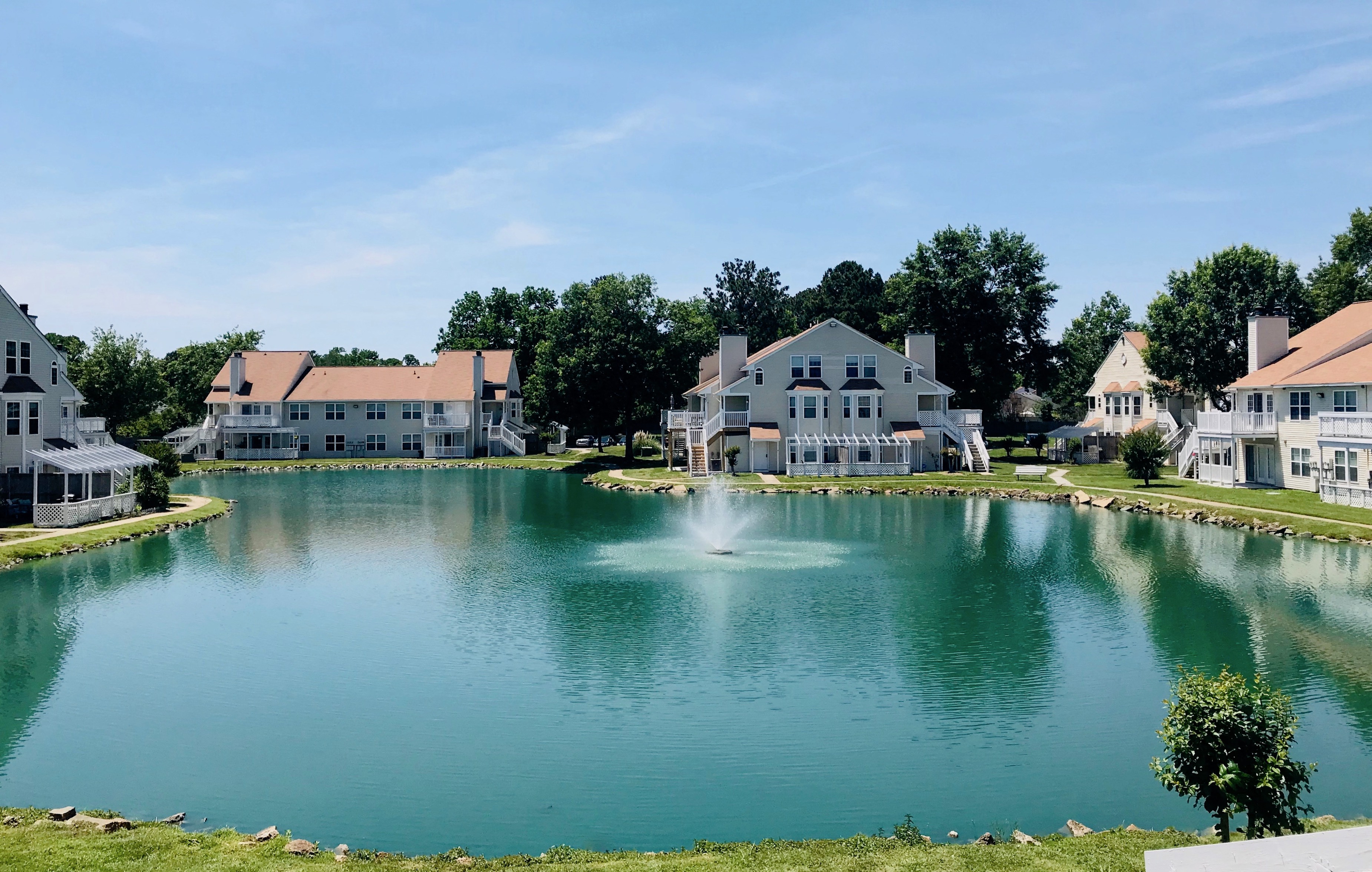 a fountain in the middle of a pond in front of houses