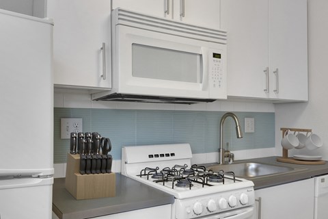 A white gas stove is in a kitchen with a white refrigerator and a white microwave above it.