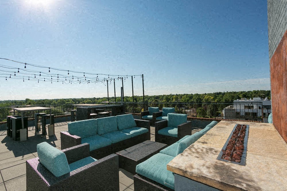 a rooftop patio with blue couches and chairs and a fire pit