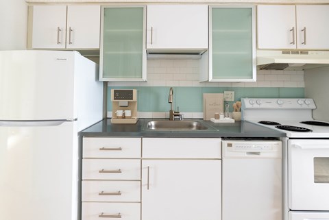 A white refrigerator is in a kitchen with white cabinets and a black counter.