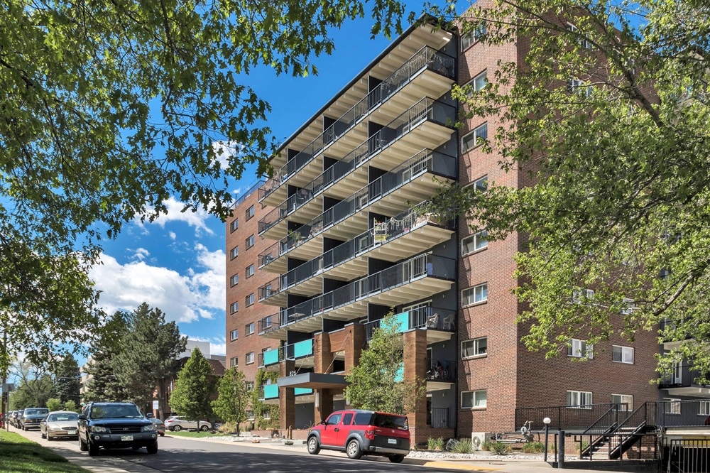 A red car is parked in front of a large apartment building.