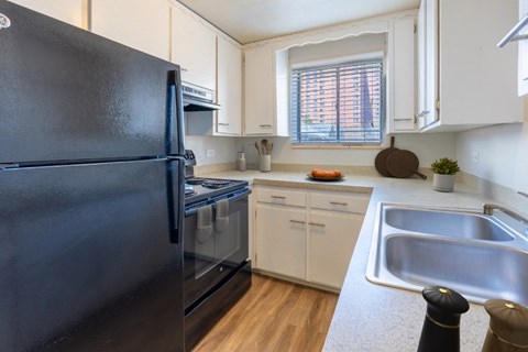 A black refrigerator is in a kitchen with white cabinets.