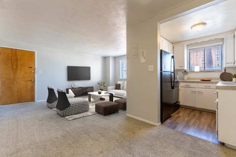 A living room with a grey carpet and a kitchen in the background.