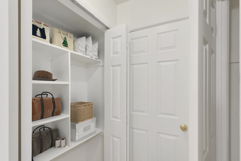 a closet with white doors and shelves with bags and purses