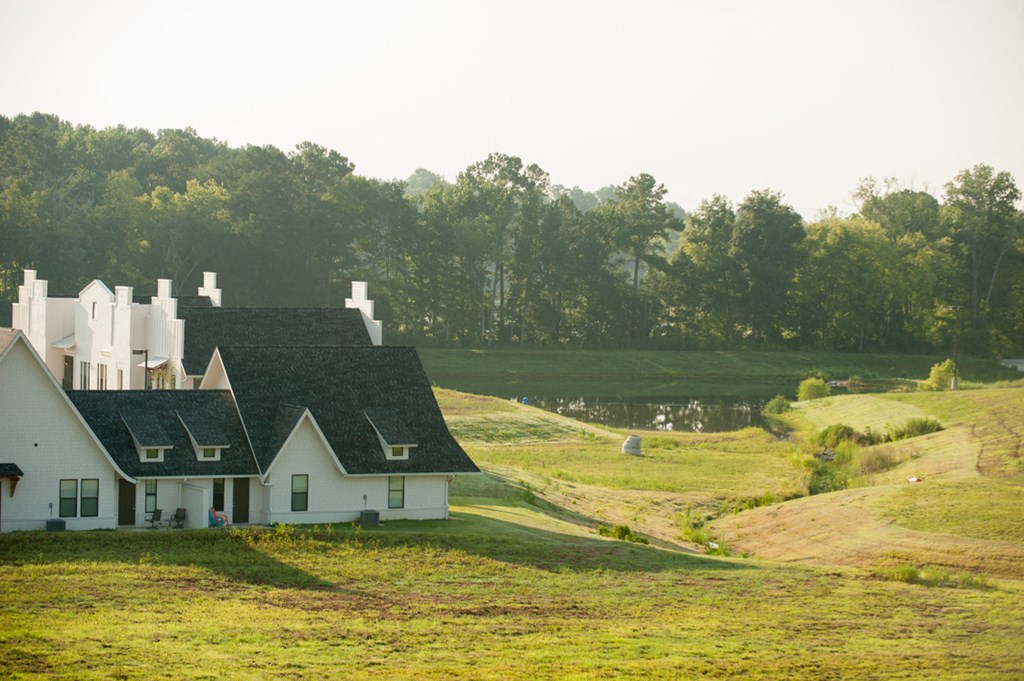a white farm house on a hill with a body of water
