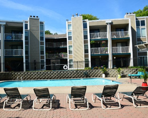 a swimming pool with chairs in front of an apartment building