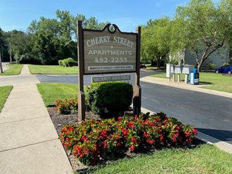 a sign for cherry street apartments in front of a flower garden