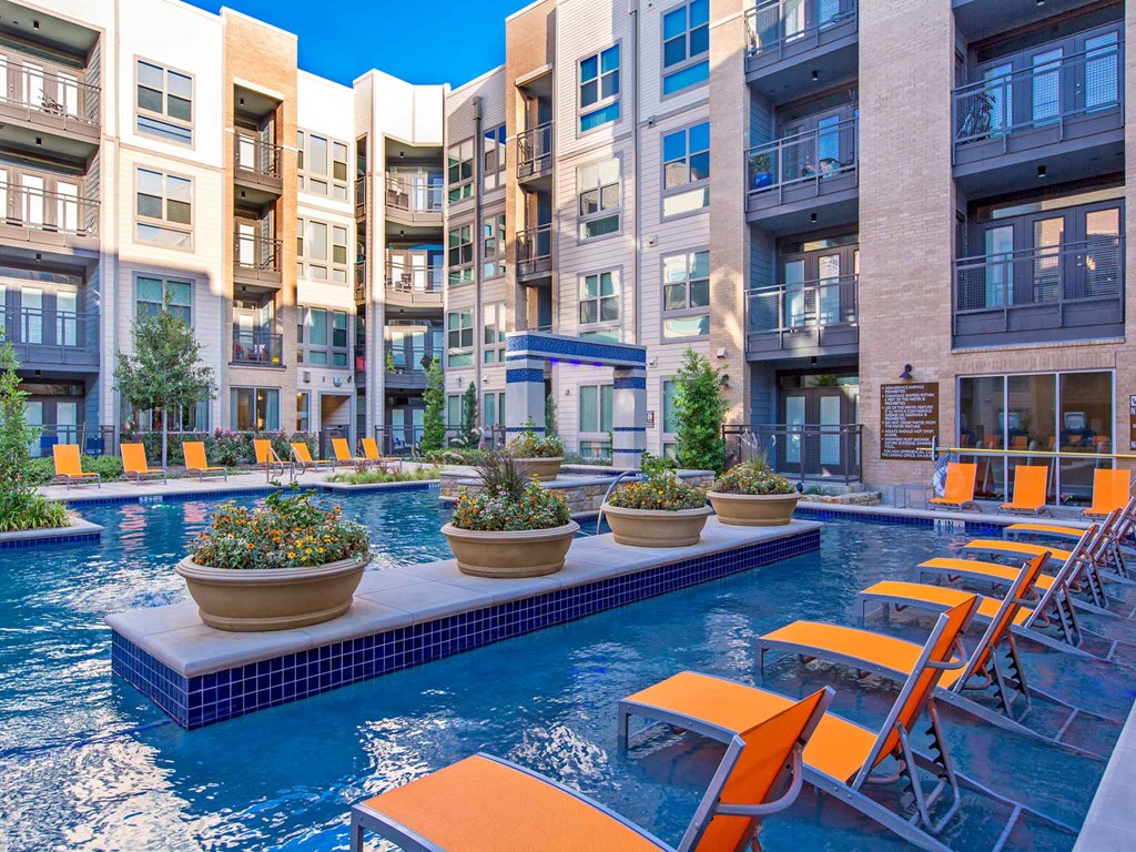 a swimming pool with orange chairs in front of an apartment building