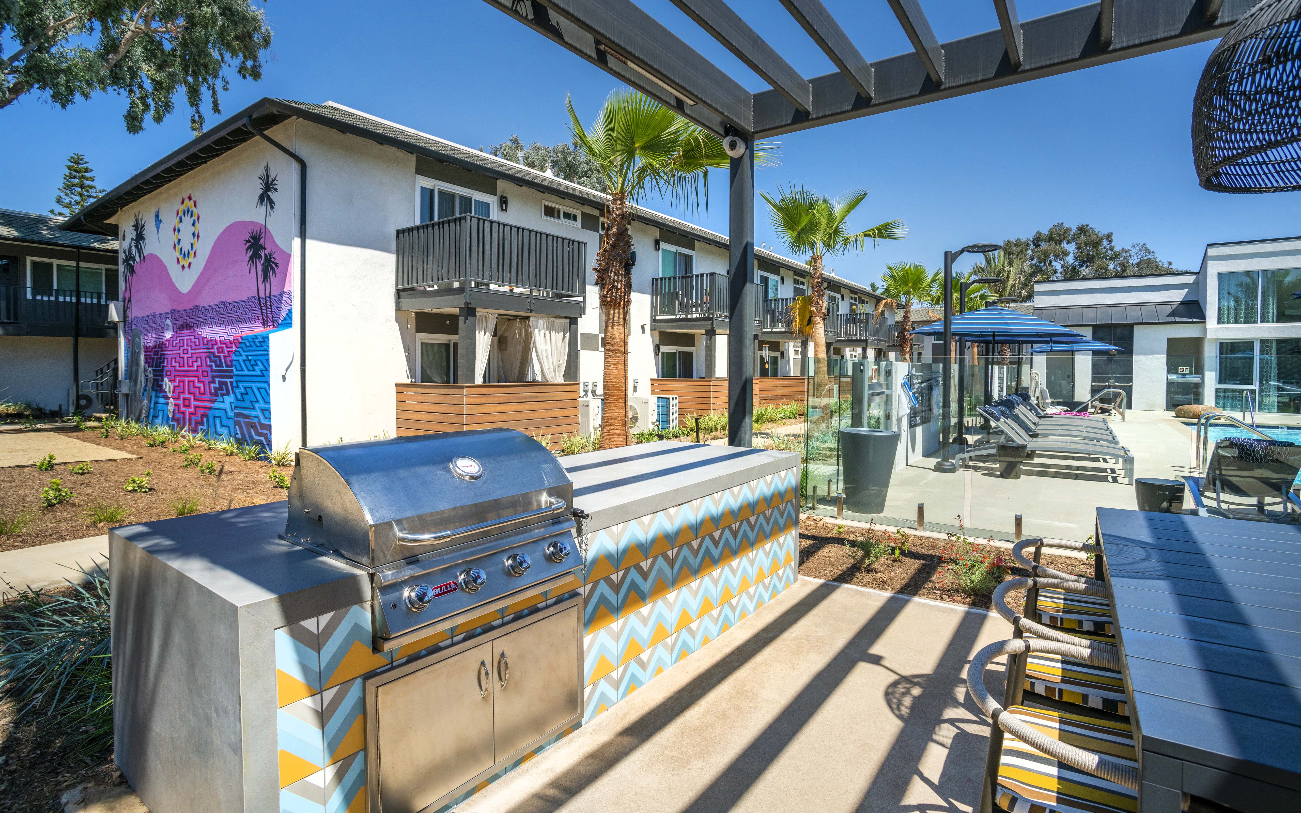 an outdoor patio with a grill and a house with palm trees
