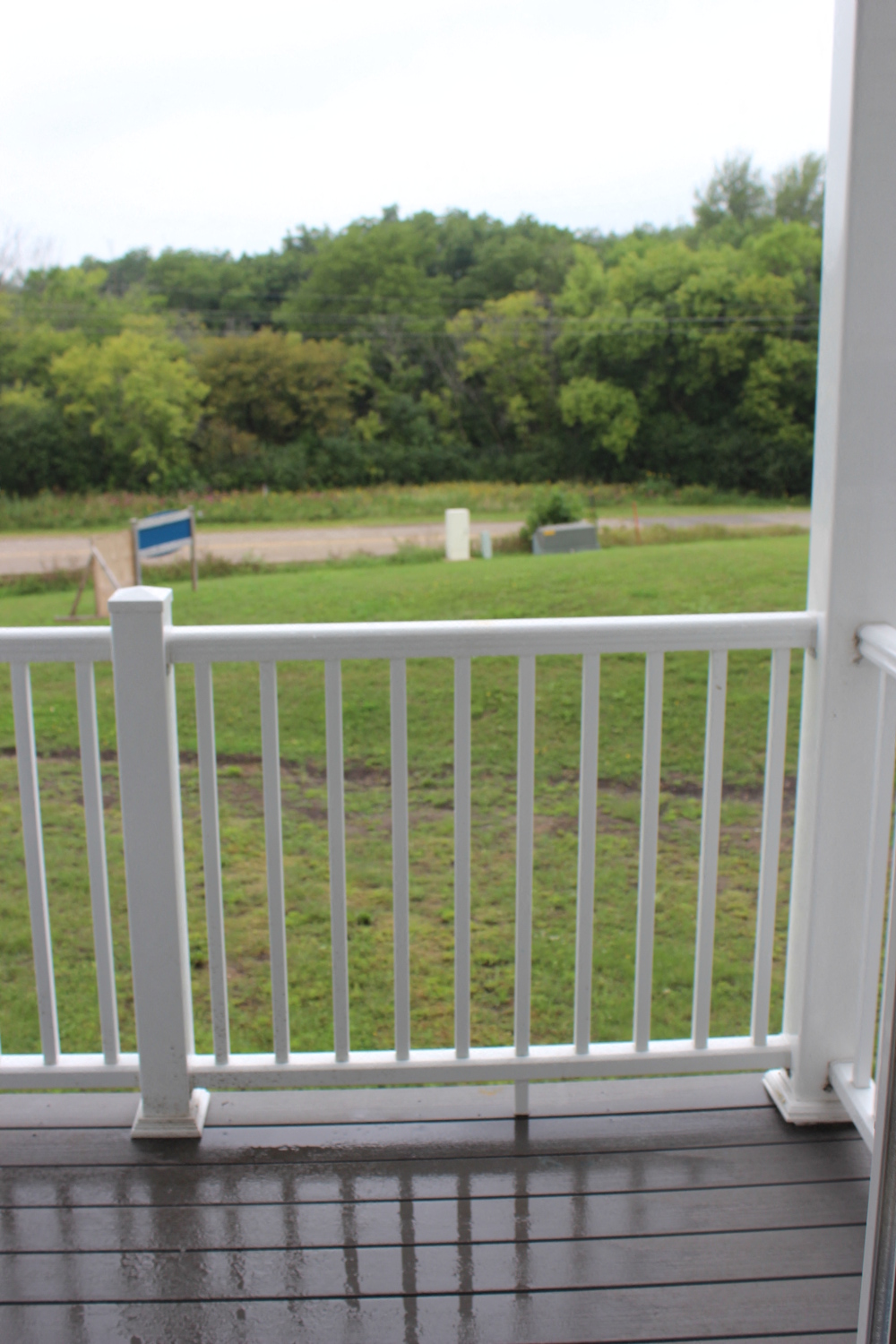 the view from the deck of a porch with white railings overlooking a grass field