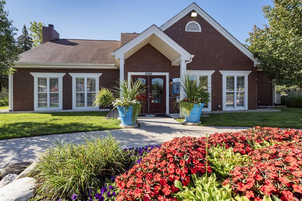 the front of a red brick house with a sidewalk and flowers
