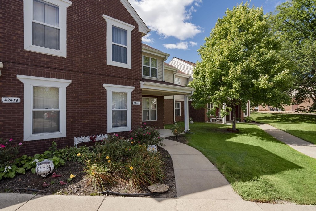a sidewalk in front of a brick building with grass and trees