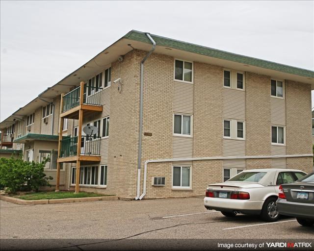 a brick apartment building with cars parked in a parking lot