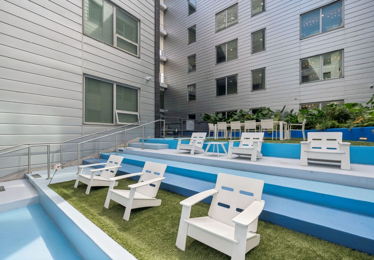 A pool with white chairs and a building in the background.