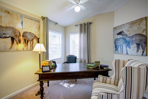 a living room with a desk and two chairs and two pictures of horses