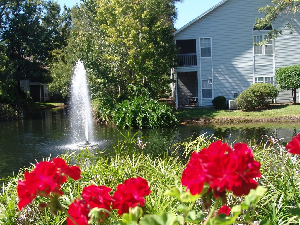 a fountain in the pond with red flowers in front of a building