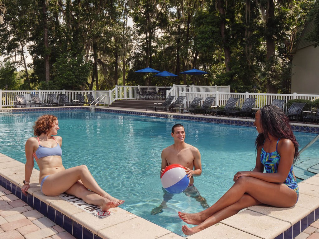 three women and a man in a pool playing with a beach ball