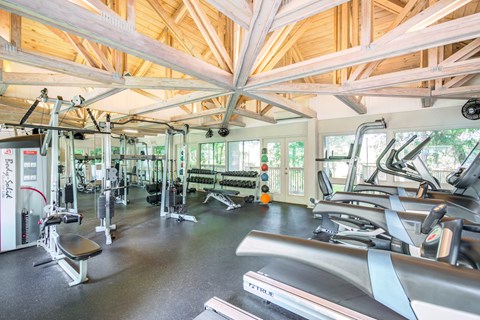 a gym with cardio equipment and weights in a building with wood ceilings