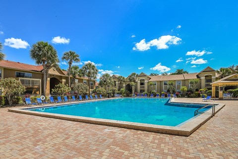 A large swimming pool surrounded by a brick patio and lounge chairs.