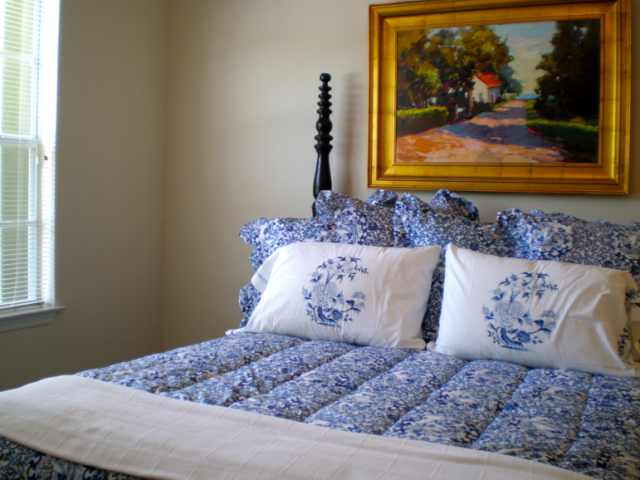 a bed with blue and white pillows with a painting on the wall above it