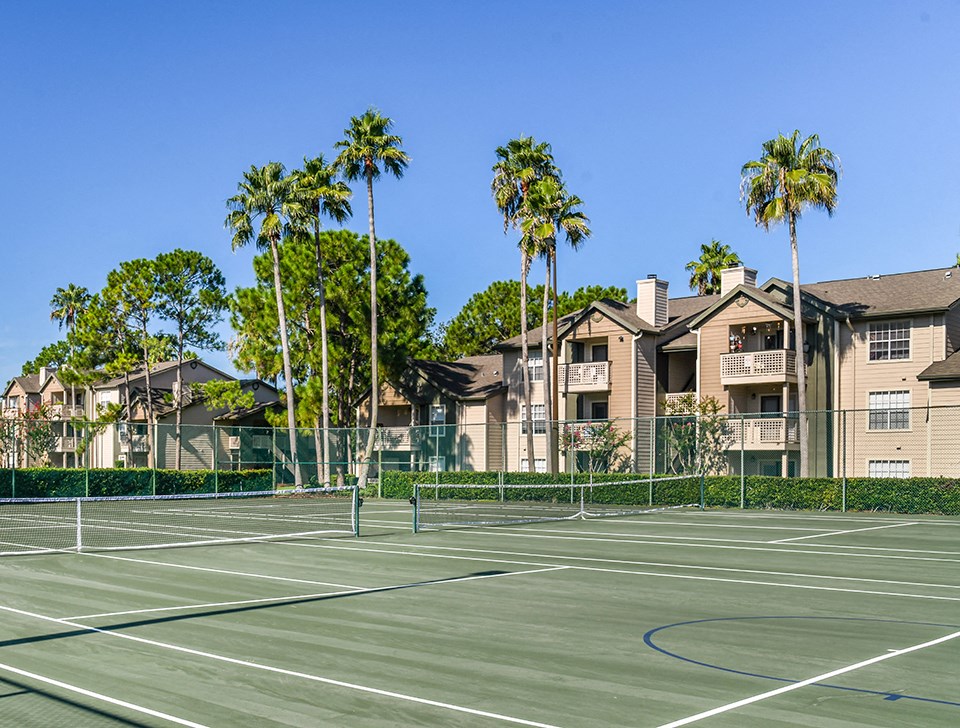 two tennis courts with palm trees and apartments in the background