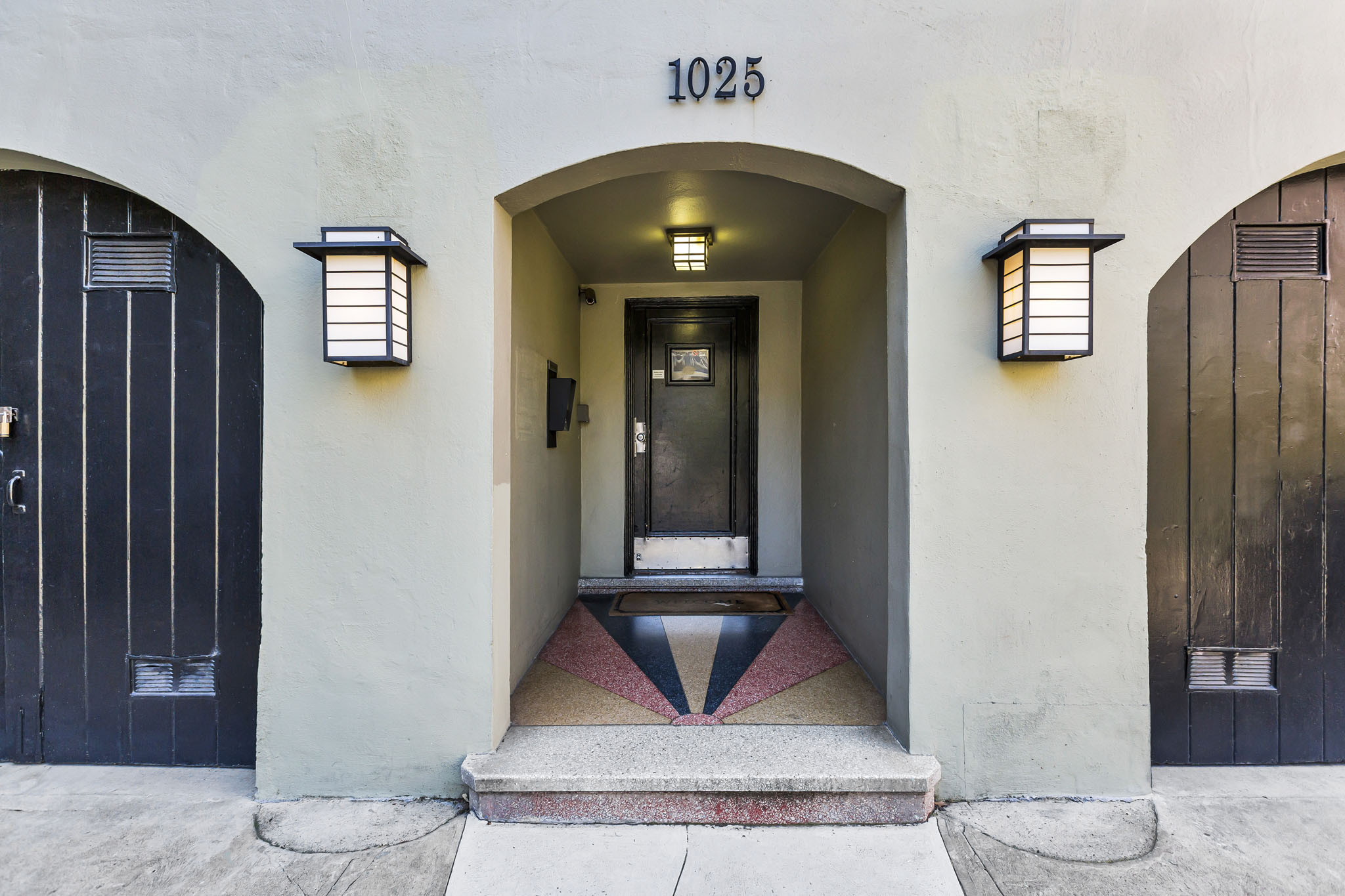 A building with the number 1025 on it has a black door and two windows with lights on them.