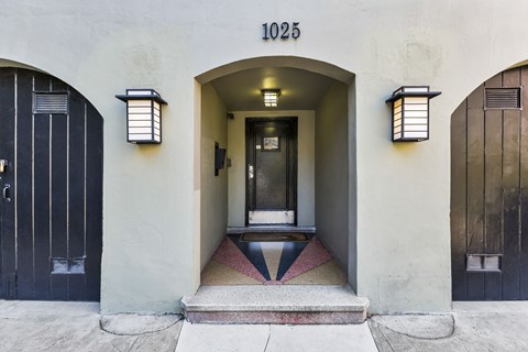 A building with the number 1025 on it has a black door and two windows with lights on them.