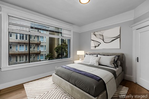 A bedroom with a large bed and a large window showing an apartment building outside.