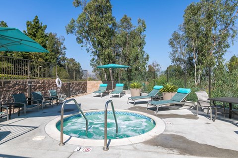 a hot tub with chairs and umbrellas in a patio with trees